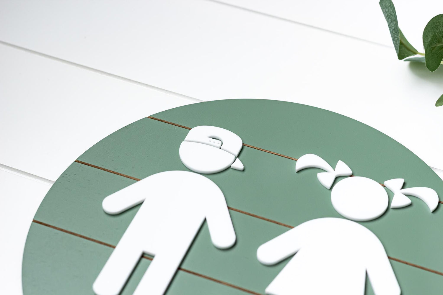 Close-up of round green 3D toddler restroom sign with white child figure details