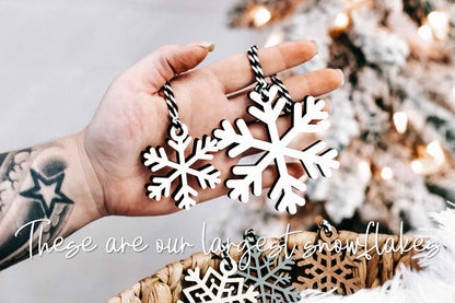 Hand holding wood snowflake ornament: white and dark layered cutout with braided string