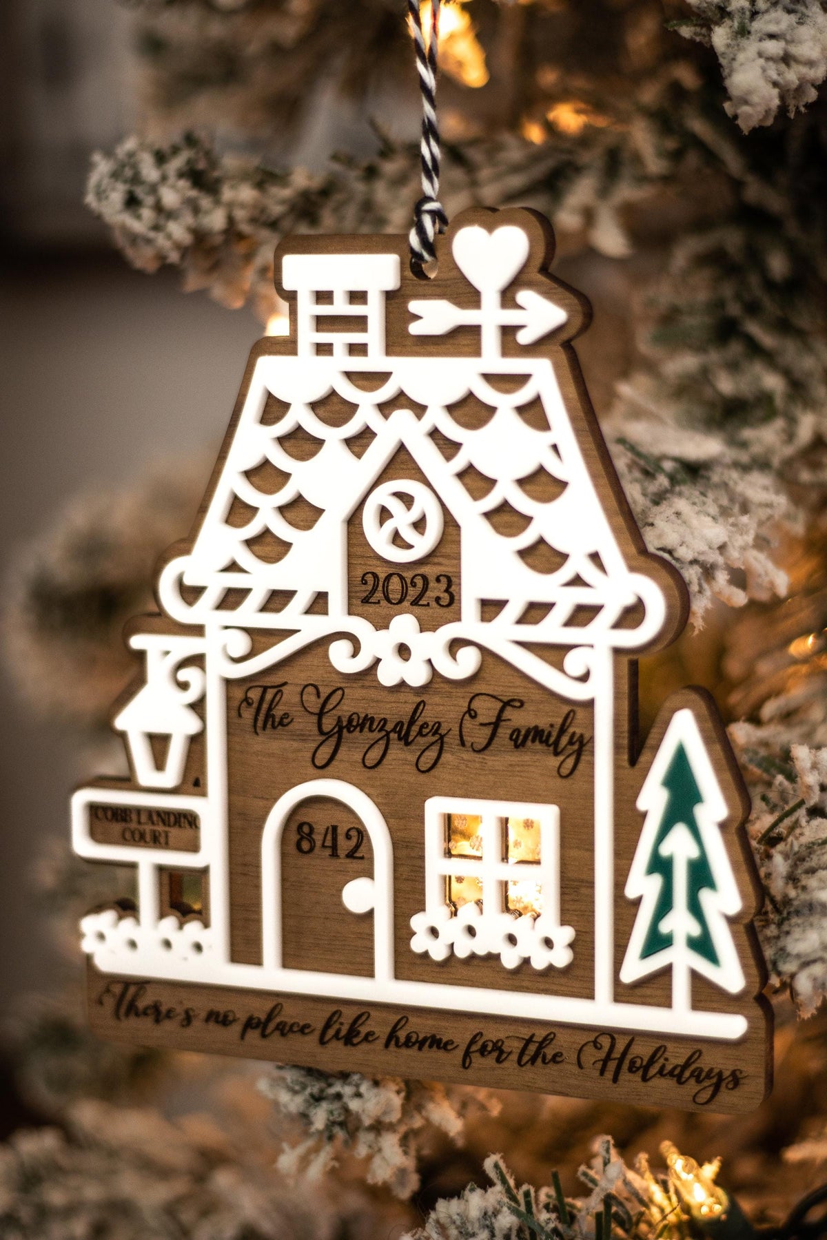 Wood gingerbread house ornament hanging on evergreen with “2023,” “Gonzalez Family,” teal tree