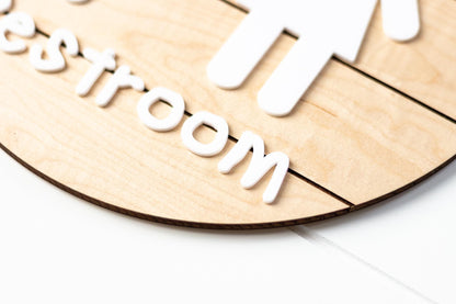 Light wood round 3D toddler restroom sign close-up with raised “Restroom” text
