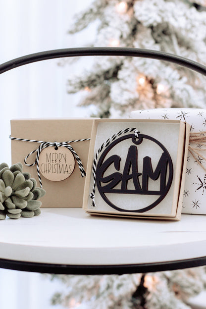 Wooden custom name ornament in open gift box, black engraving on round tag