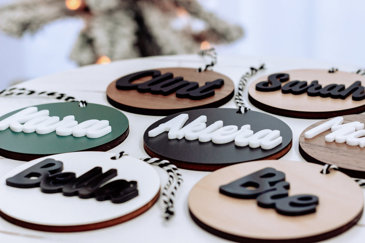 Round wooden name ornaments with rope hangers, featuring white and black lettering on colored faces