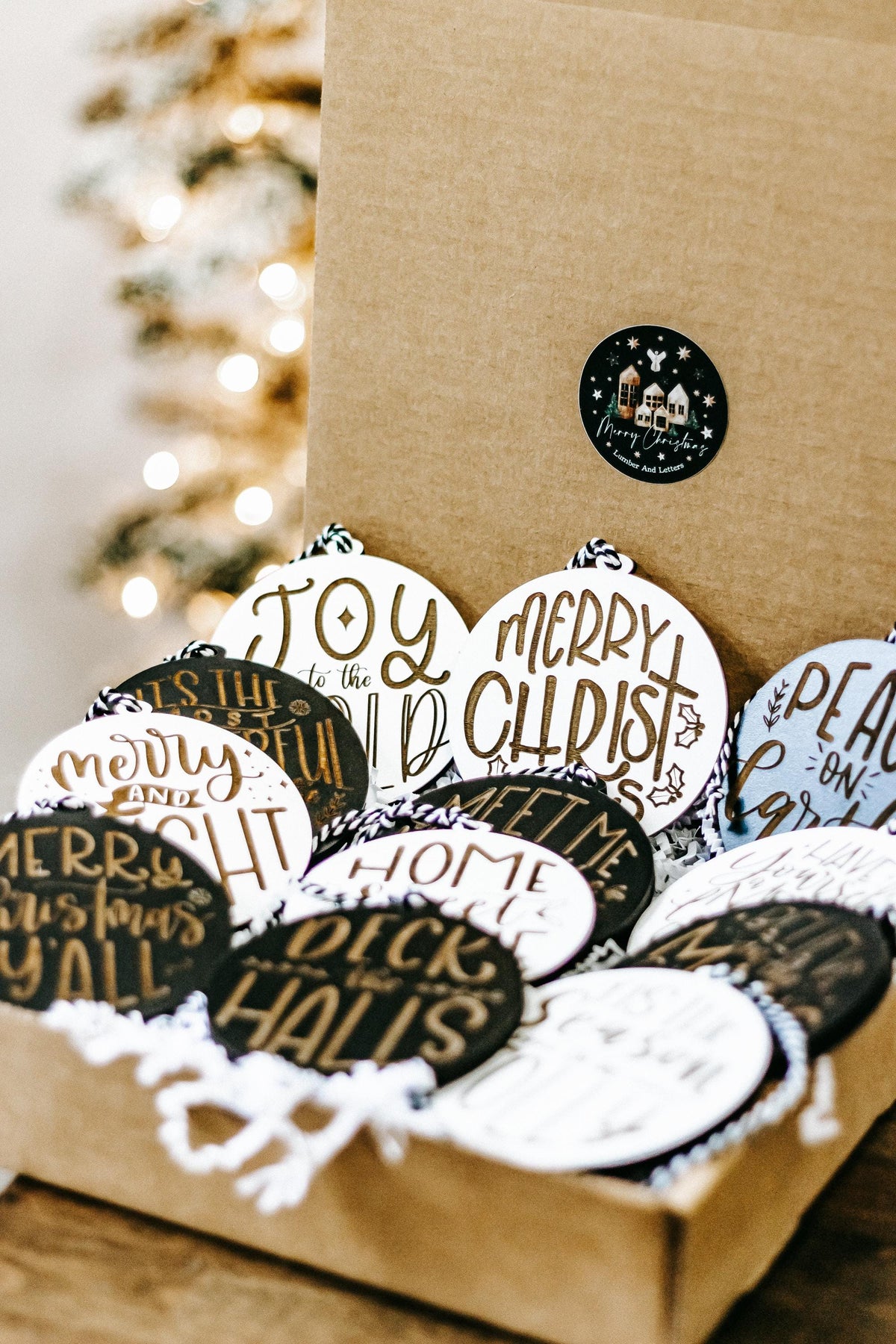 Set of engraved Christmas ornaments in a kraft gift box, black and white rounds with gold text.