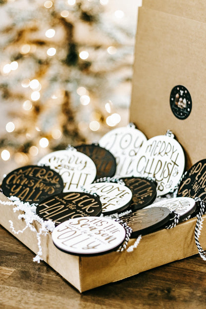 Engraved Christmas ornament set in a gift box, black and white discs with gold lettering.
