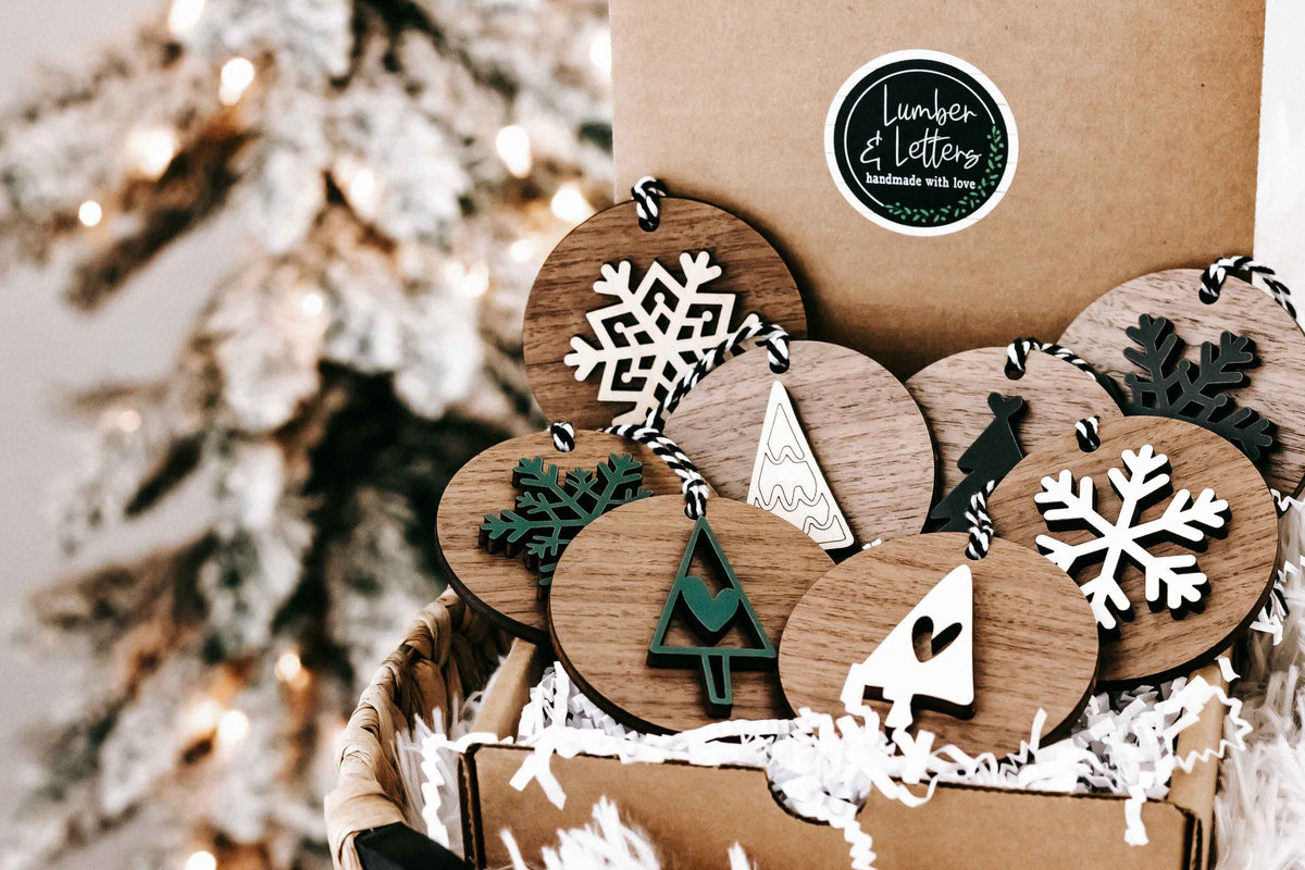 Wooden Christmas ornaments with snowflake, tree, and star designs in a kraft gift box