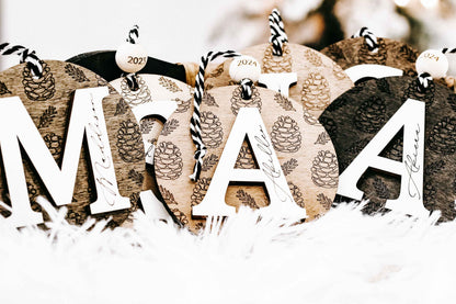 Set of round engraved pine cone ornaments with zebra-striped loops and year tags 2024