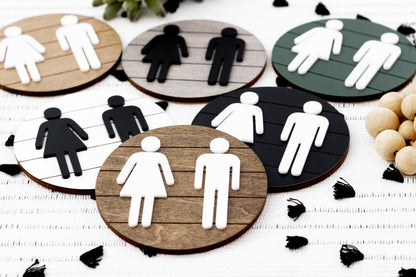 Assorted directional restroom signs with female and male icons on round dark and wood backgrounds