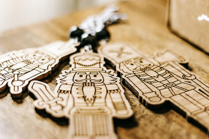 Close-up of engraved wooden nutcracker ornaments in a gift box with dark bead cords