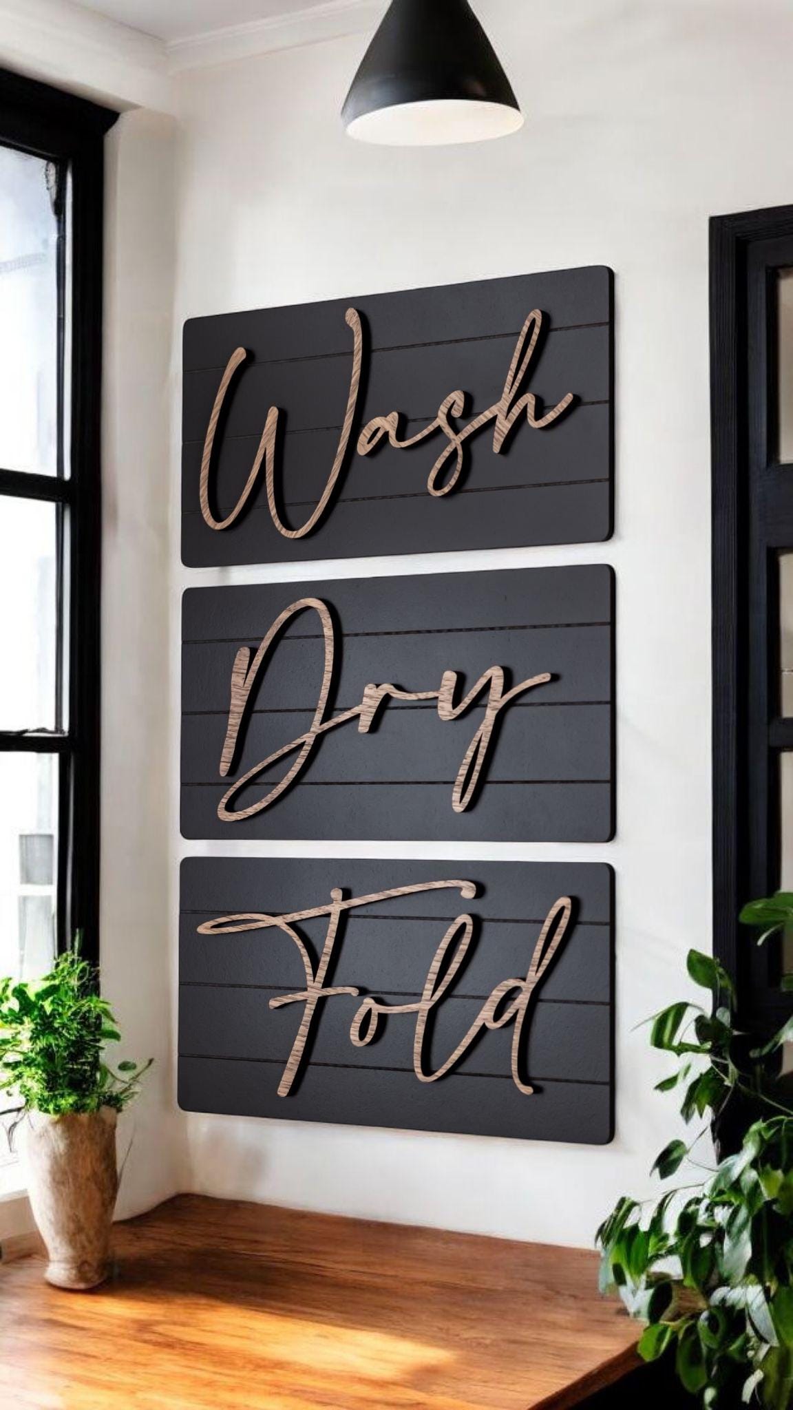 Three dark wall signs reading Wash, Dry, Fold with wood-tone cursive lettering on wall