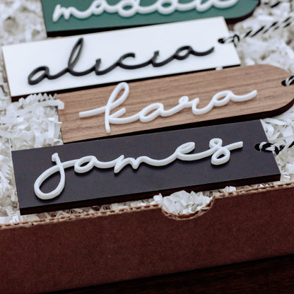 Personalized wooden name tags in white script on wood planks, multiple colors