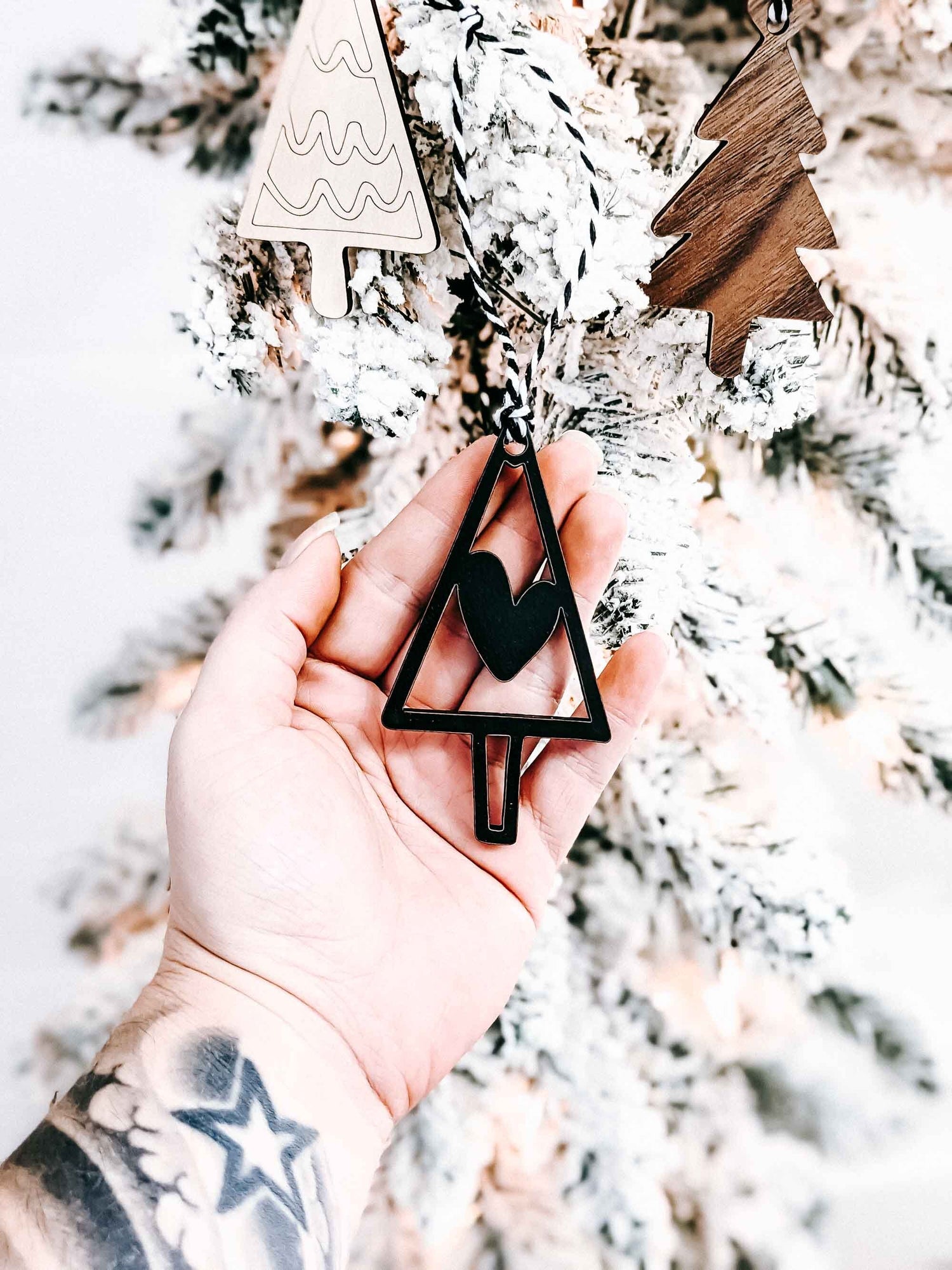 Hand holding boho Christmas tree ornaments: wood and black triangle trees with striped rope hangers