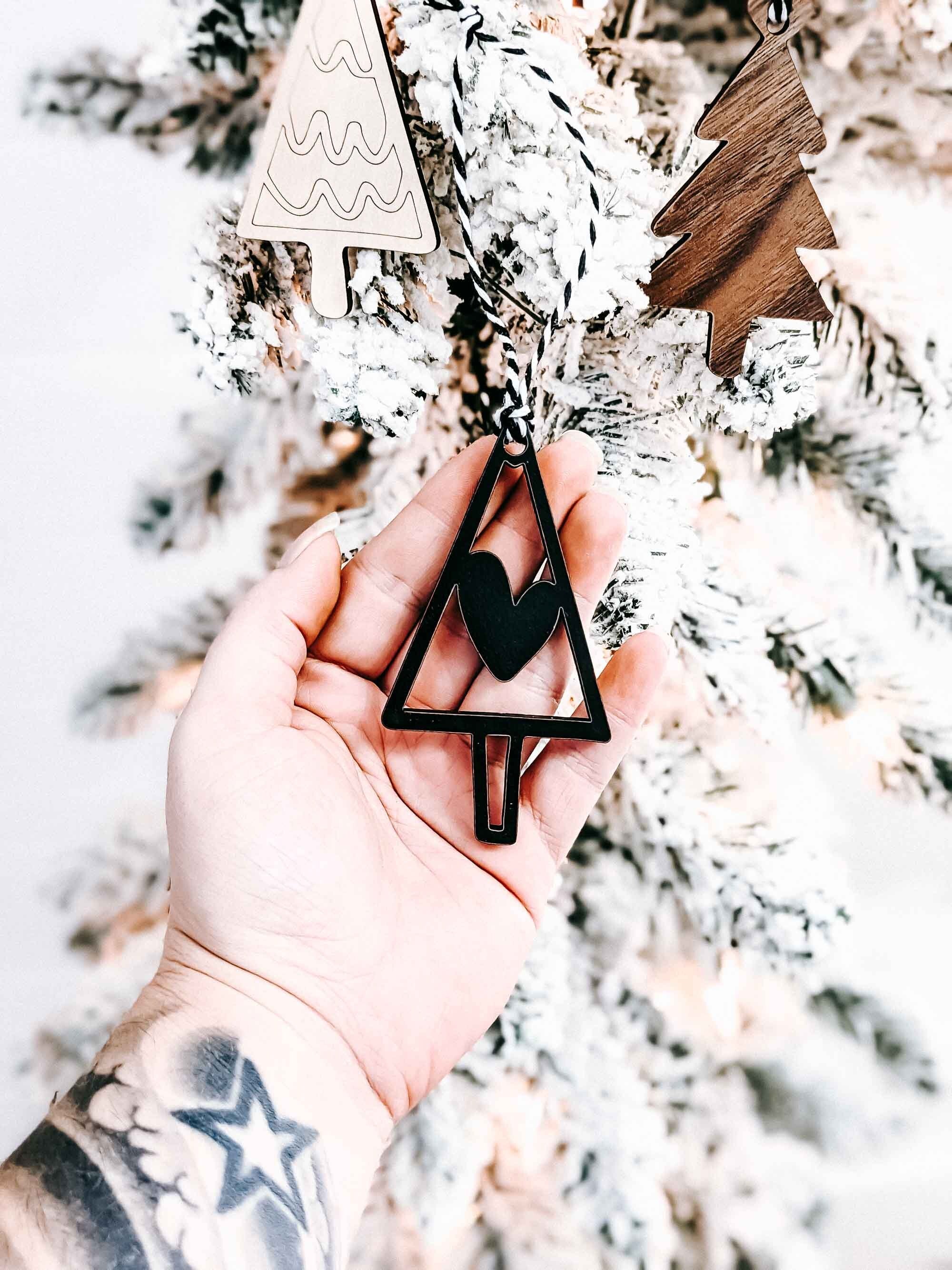 Hand holding boho Christmas tree ornaments: wood and black triangle trees with striped rope hangers