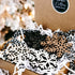 Snowflake wooden ornaments in a kraft box, with black and white cutout designs and string ends