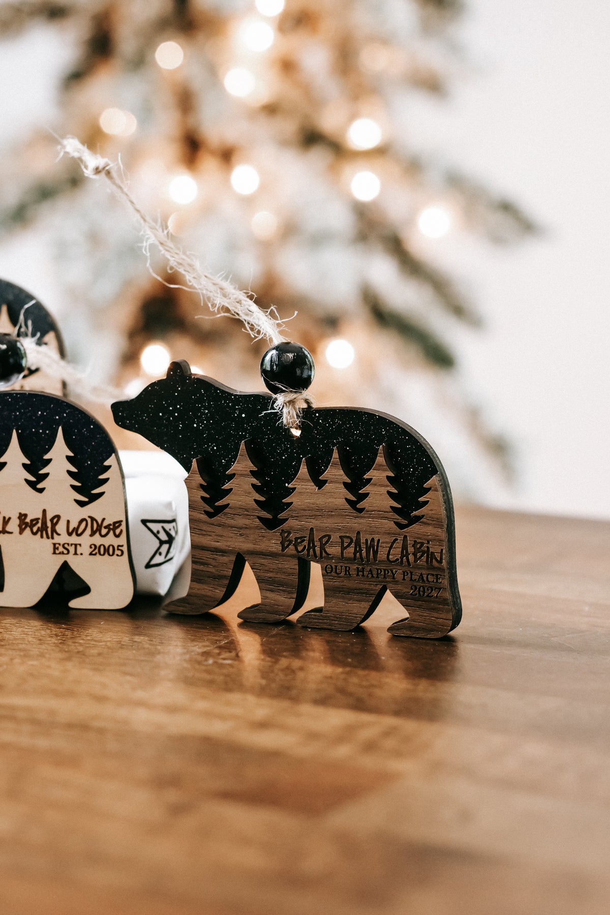 Angled view of dark glitter bear cabin ornaments with engraved pine trees and text