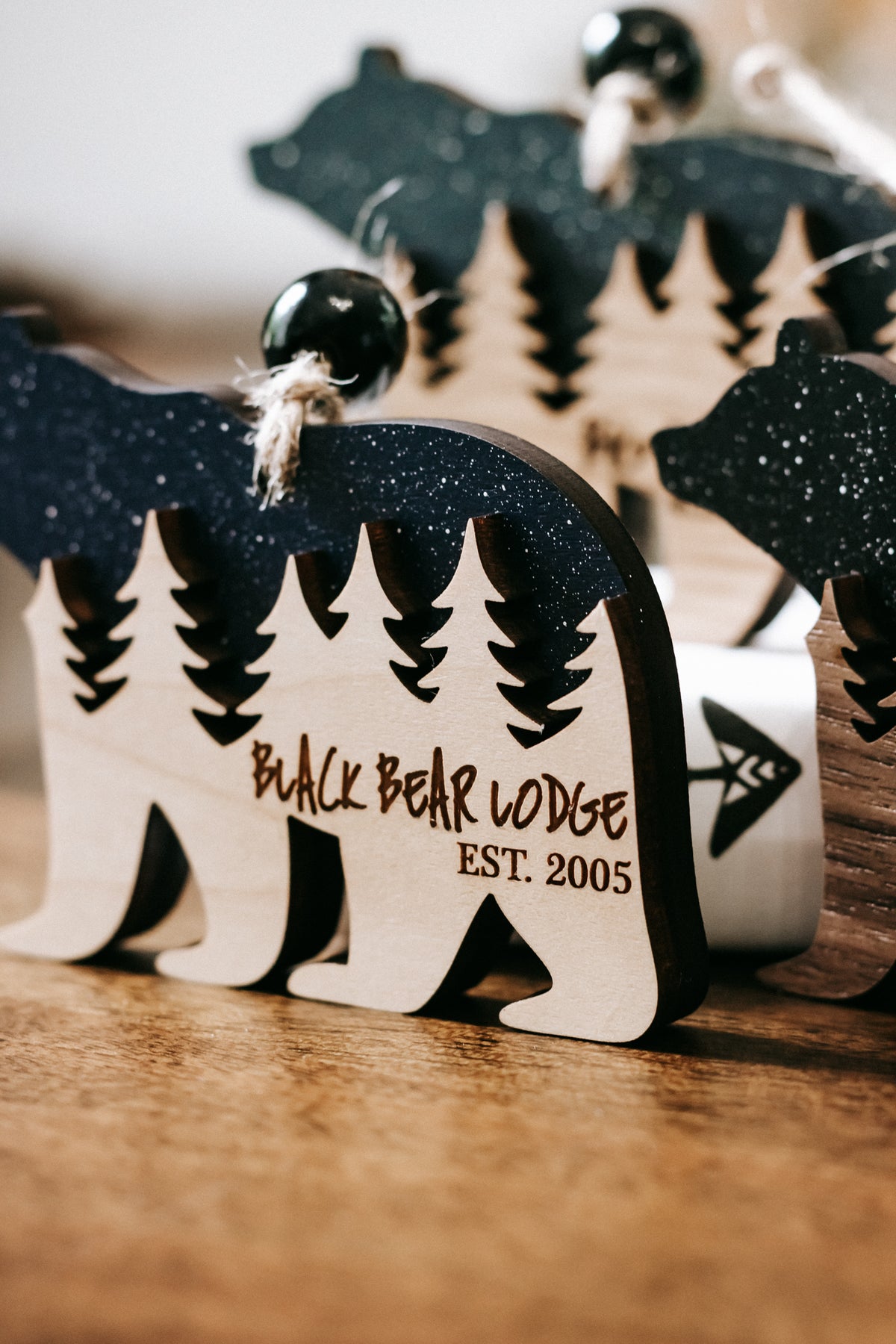 Close-up bear cabin ornament with dark glitter finish, pine trees, and engraved text