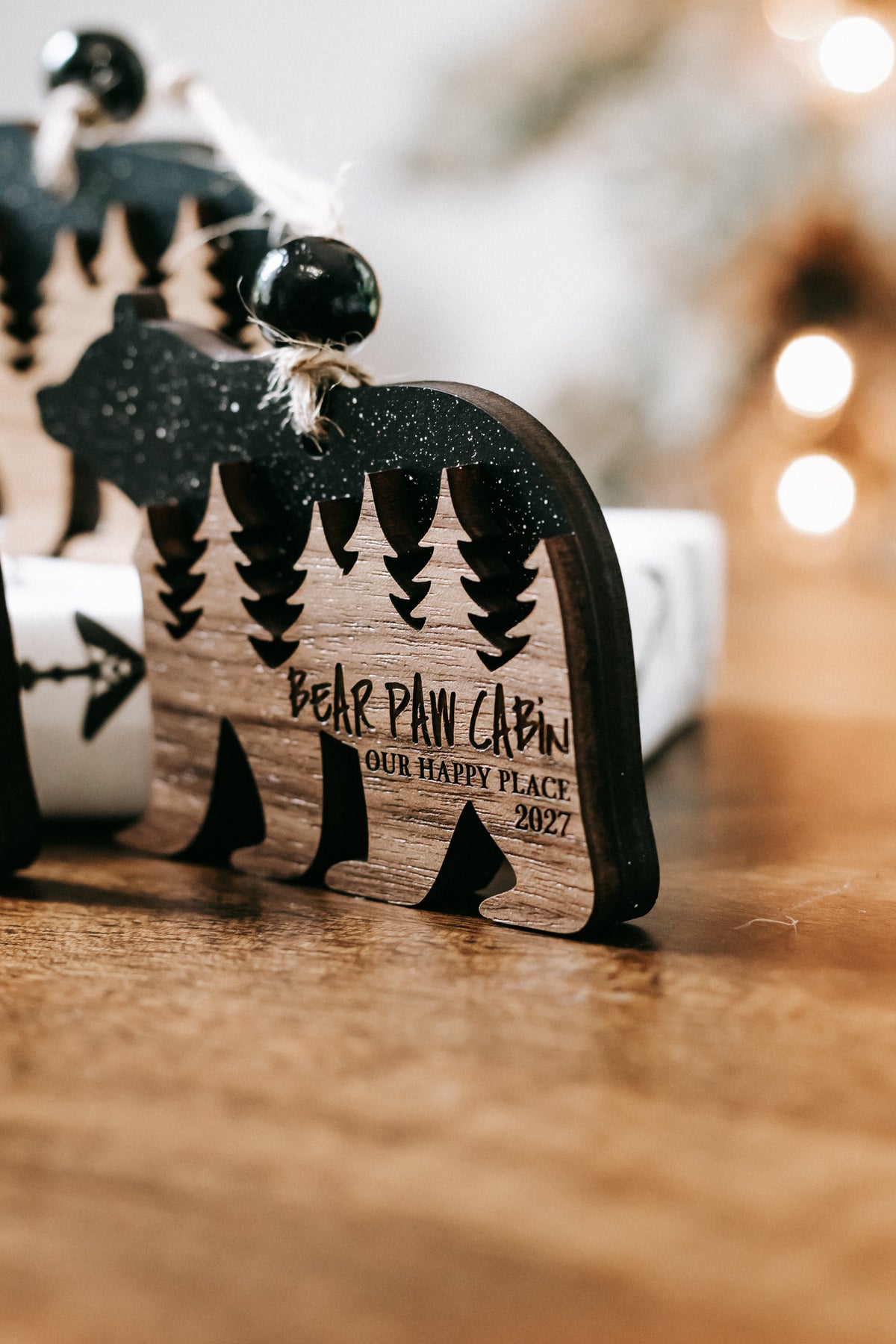 Bear cabin ornament close-up with dark glitter bear, engraved pine trees, and text