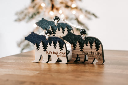 Two dark glitter bear-shaped cabin ornaments with engraved forest scene and lettering