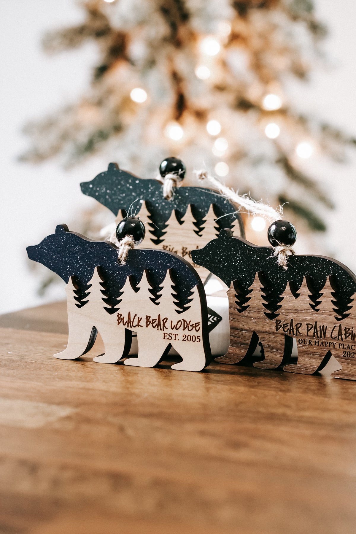 Two bear cabin ornaments standing side by side with engraved pine trees and cabin text