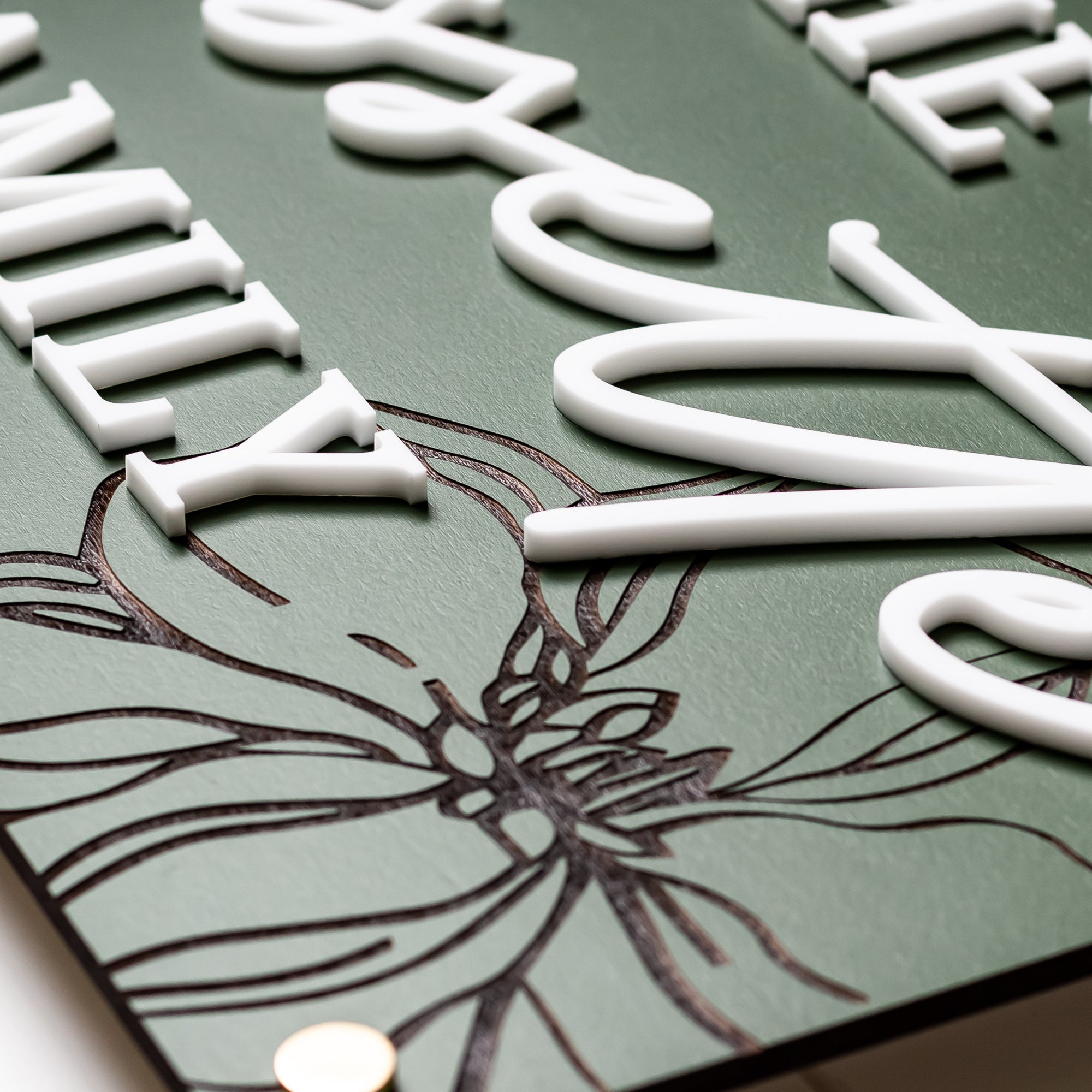 Green rectangle family name sign with white engraved letters and floral line art