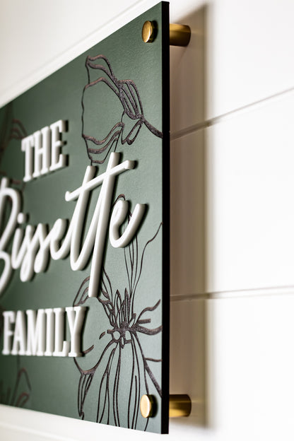 Green wall-mounted rectangle family sign with engraved white script and floral outline