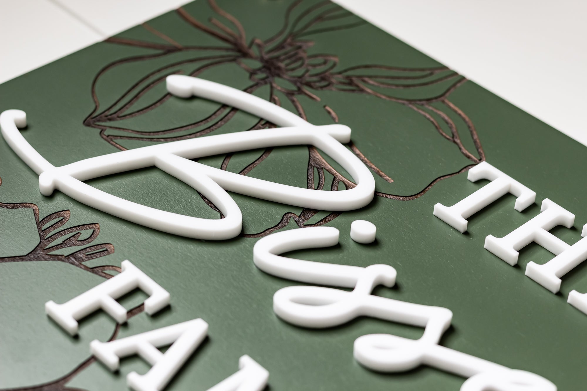 Green rectangle family name sign with white cursive letters and floral linework
