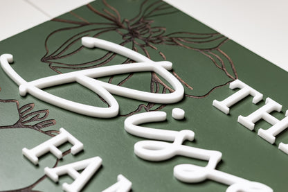 Green rectangle family name sign with white cursive letters and floral linework