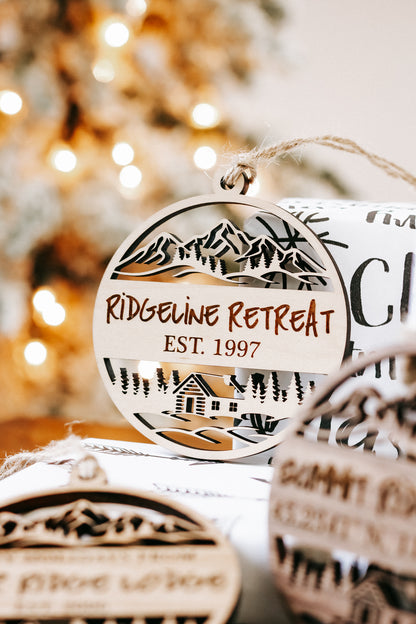 Round engraved wood ornament showing mountain cabin scene and “Riderline Retreat”