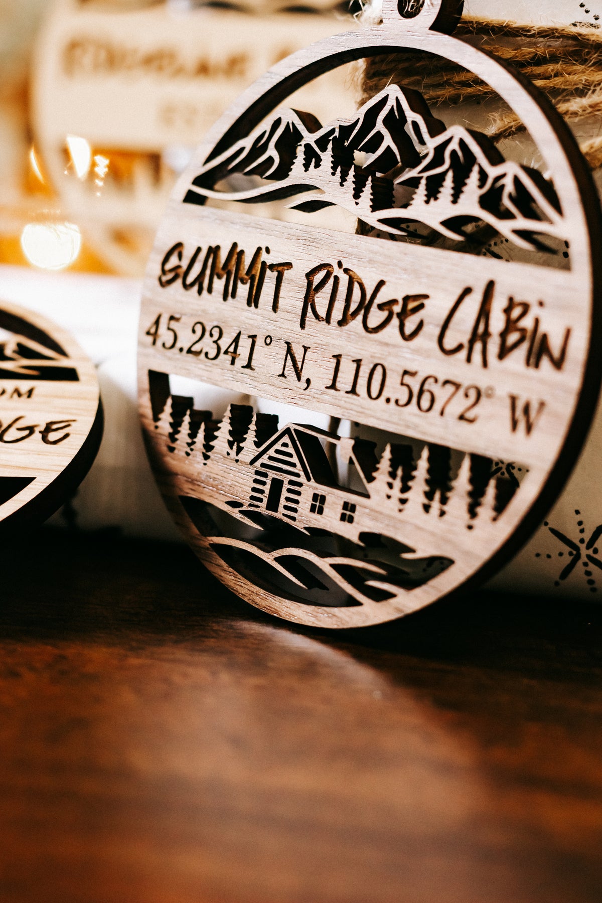 Close-up round engraved wood ornament reading “Summit Ridge Cabin” with coordinates