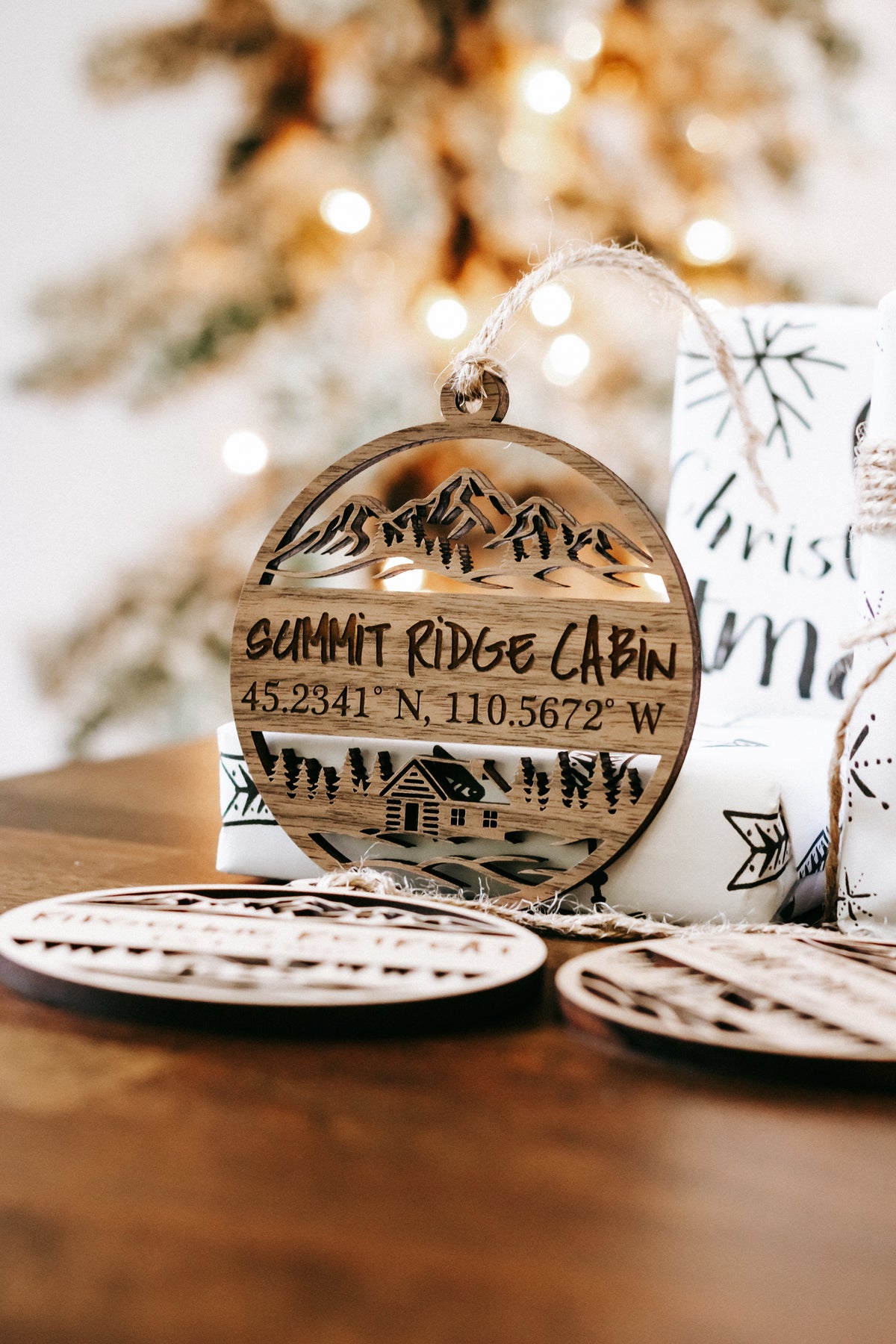 Round engraved wood cabin ornament with mountains, coordinates, and hanging twine