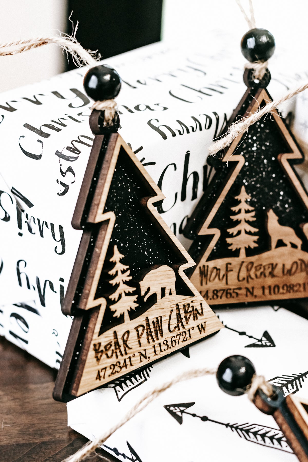 Set of wooden tree-shaped ornaments with hanging beads and printed cabin details on white backs.