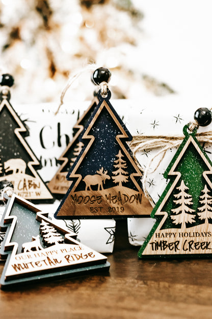 Mixed wooden tree ornaments with hanging beads, dark green centers, and printed cabin names.