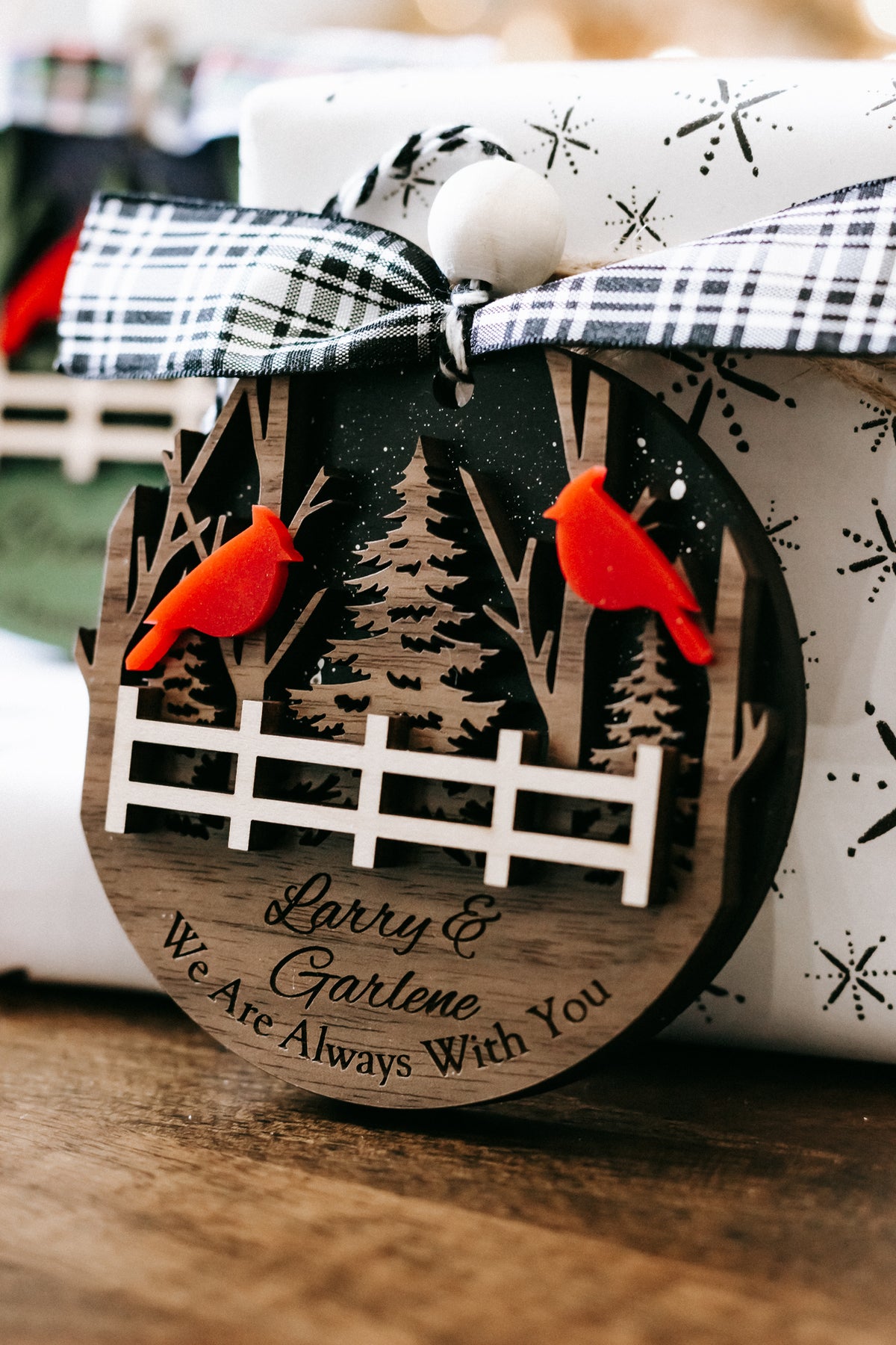 Personalized memorial ornament closeup with red cardinals, forest trees, plaid bow