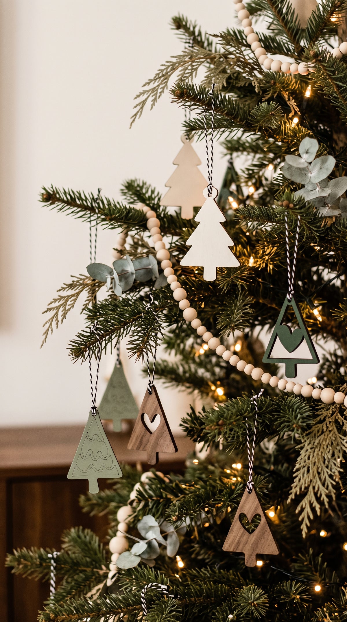 Farmhouse Christmas tree ornaments hanging on evergreen branches, tree and heart shapes with strings