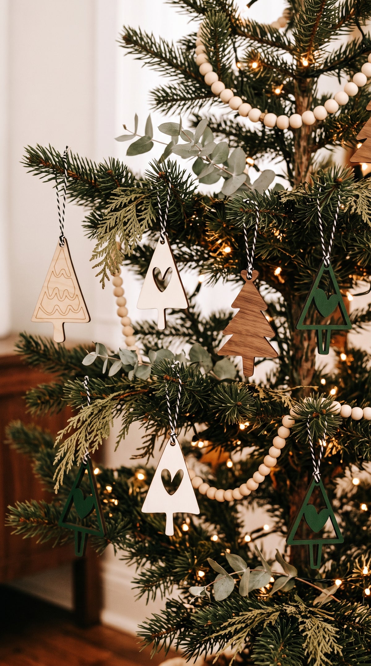 Wooden Christmas ornaments hanging on a decorated tree: white triangles and green trees