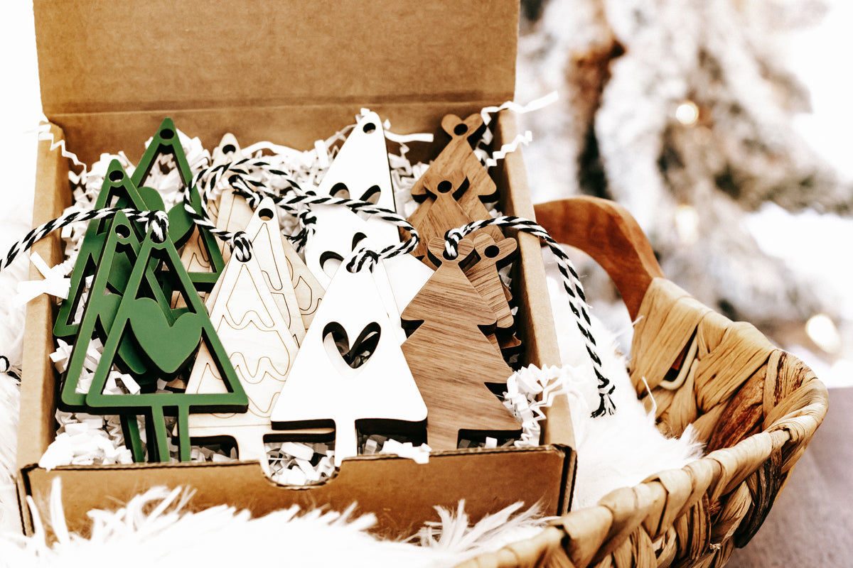 Set of wooden Christmas ornaments in a gift box with green trees, white triangles, and rope hangers