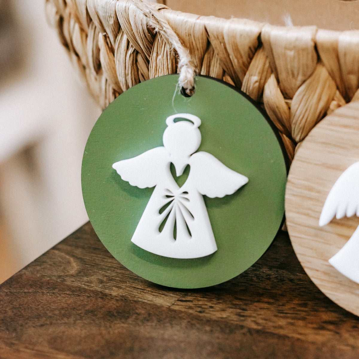 Close-up of green round angel ornament with white dress and wings, twine hanger loop