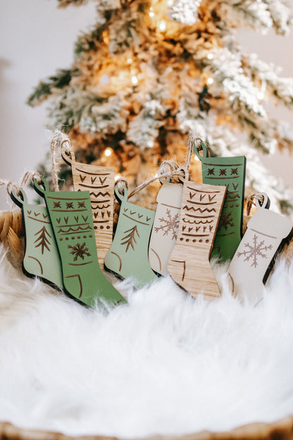 Engraved wooden stocking ornaments with green, cream, and wood designs on a snowy display