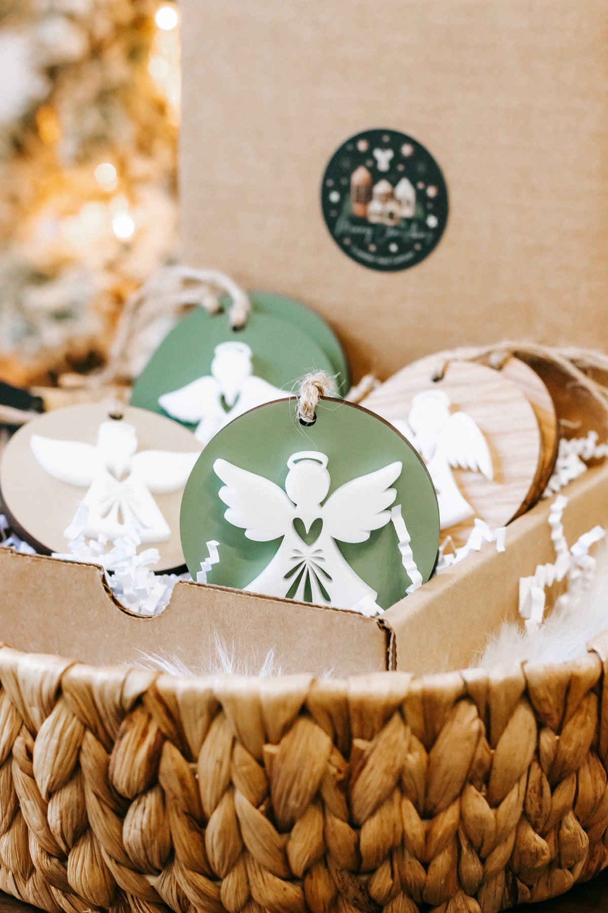 Layered angel ornament with green and white wings on round disc, hanging on twine