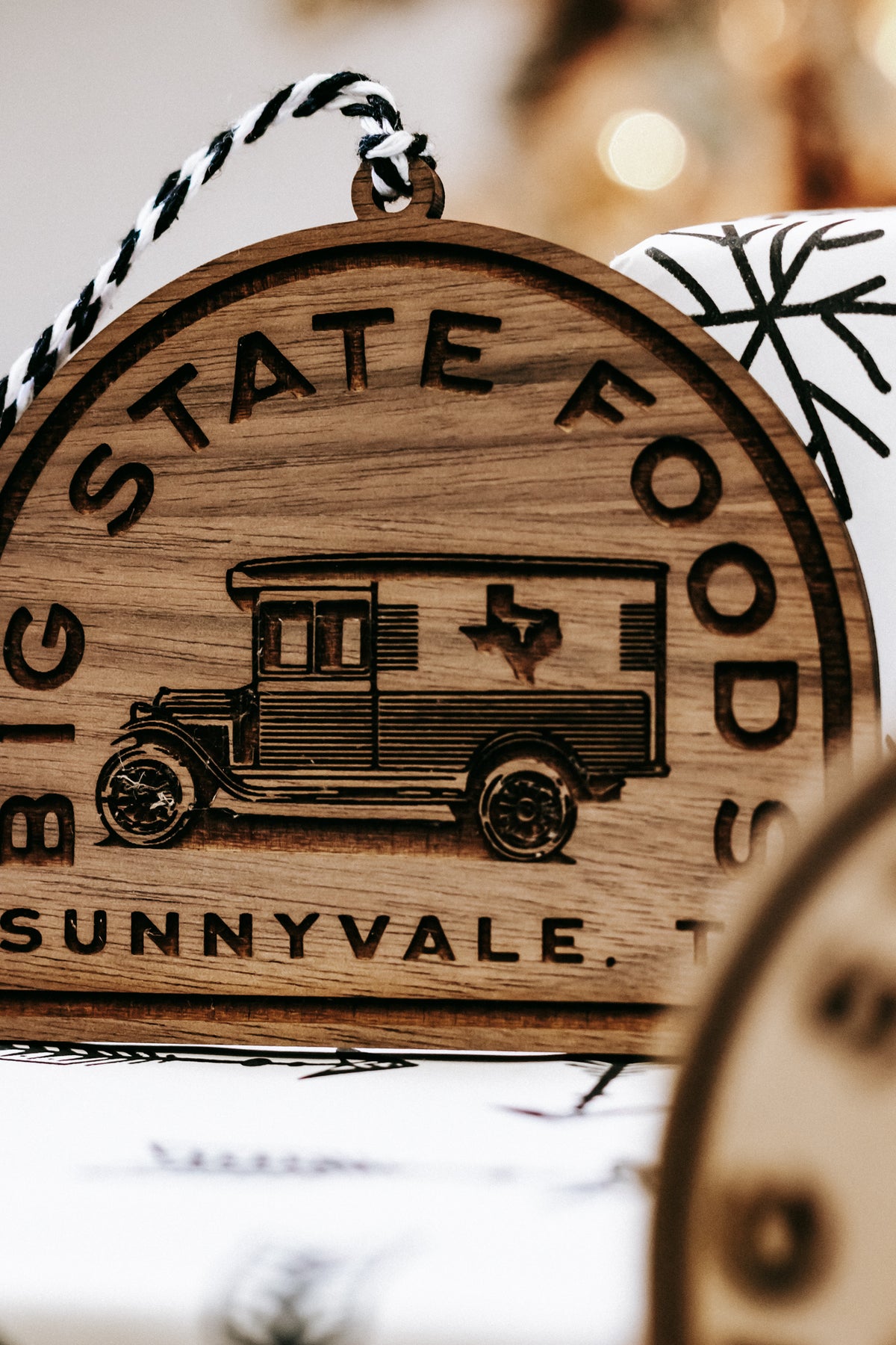 Tight view of wooden ornament with van illustration and “STATE FOODS” text around border.