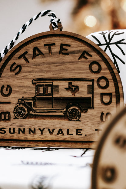 Tight view of wooden ornament with van illustration and “STATE FOODS” text around border.