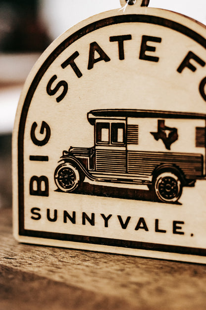 Wooden ornament close-up with van graphic and “BIG STATE FOODS / Sunnyvale” lettering.