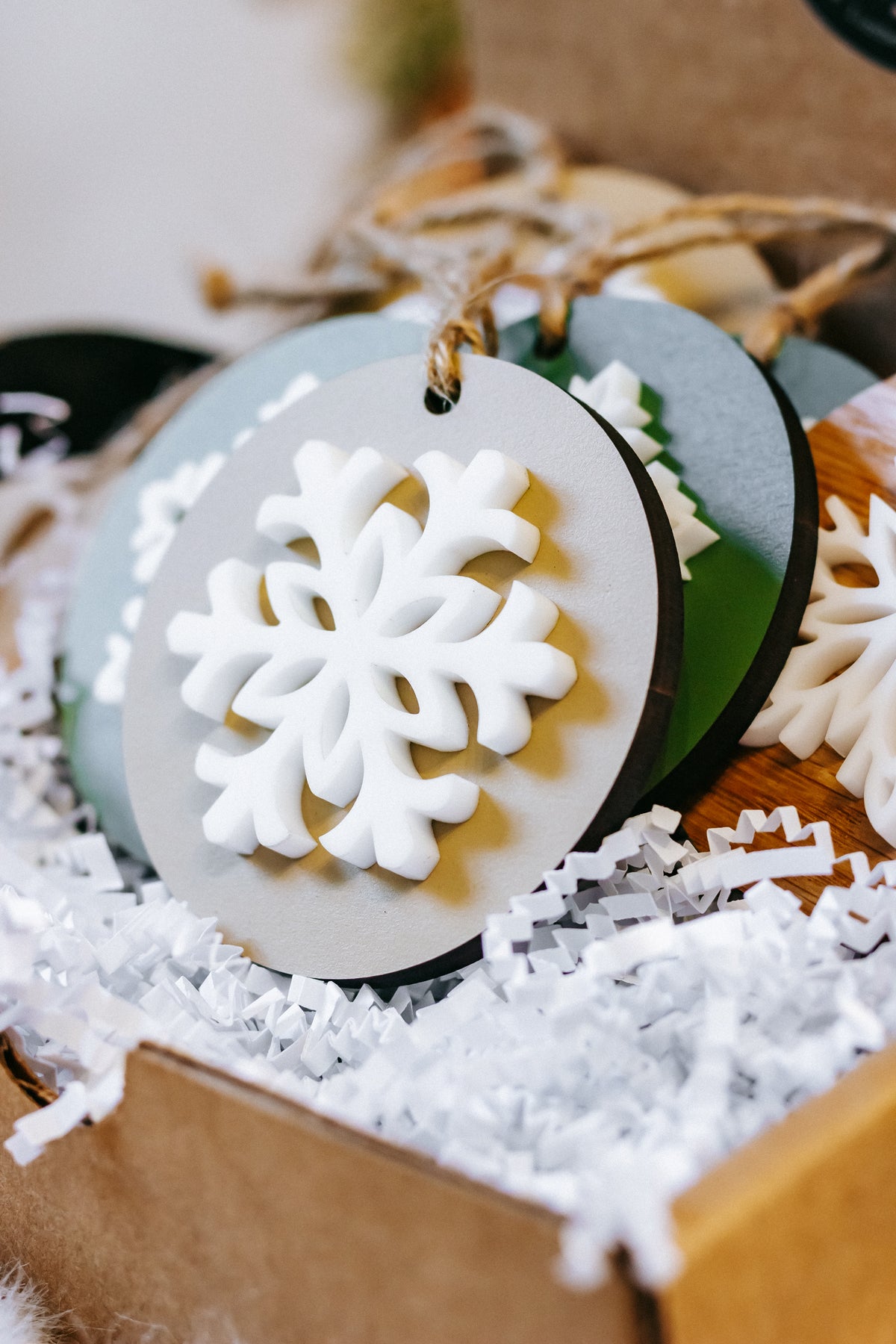 Round snowflake ornament with dark green base and raised white snowflake cutout, twine hanger
