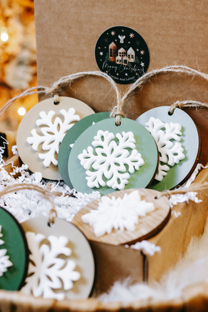 Close-up of round wooden snowflake ornaments with green base and white snowflake design, twine