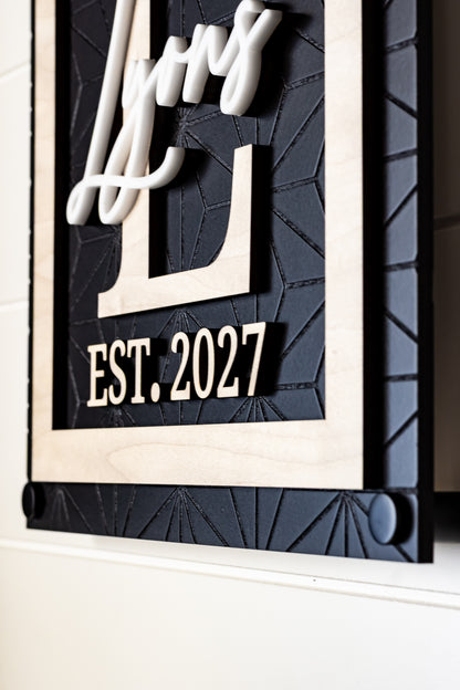 Rectangle family name sign with white cursive letters and "EST. 2027" on dark geometric panel