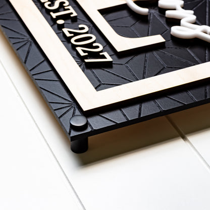 Rectangle family name sign with light wood frame and four black corner posts on dark board
