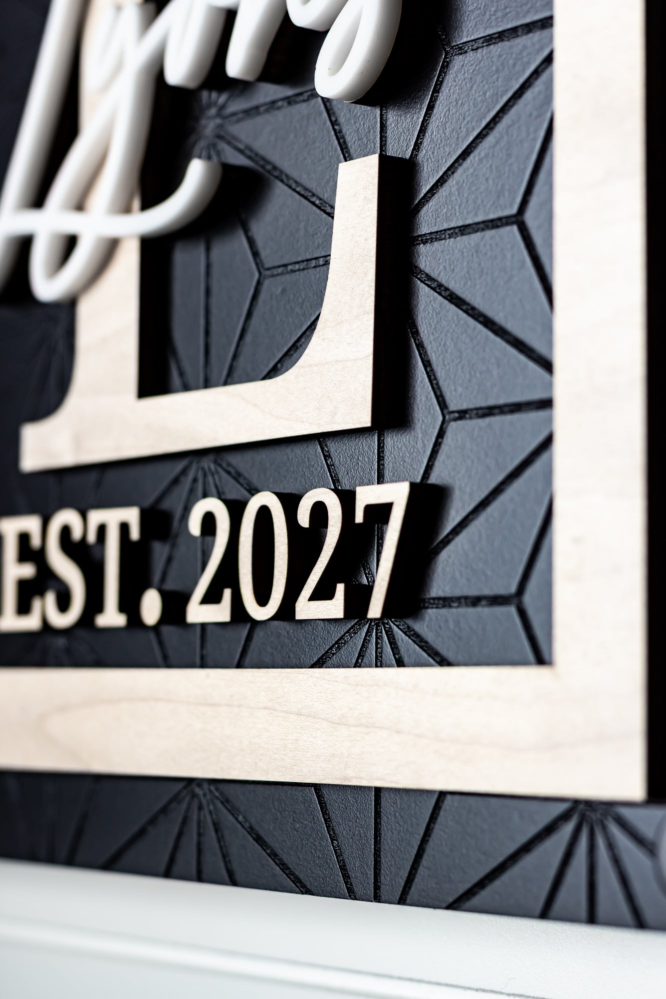 Rectangle family name sign detail with "EST. 2027" text and white cursive letters on dark panel