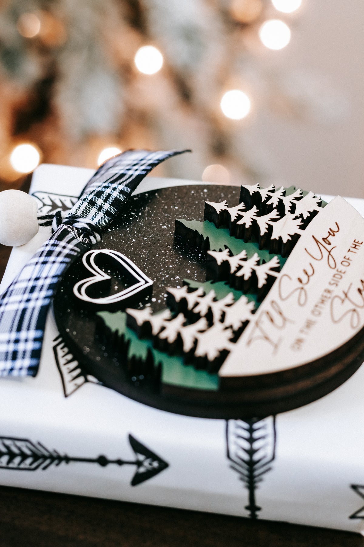 Memorial Christmas ornament close-up with plaid bow, heart icon, and pine forest artwork.
