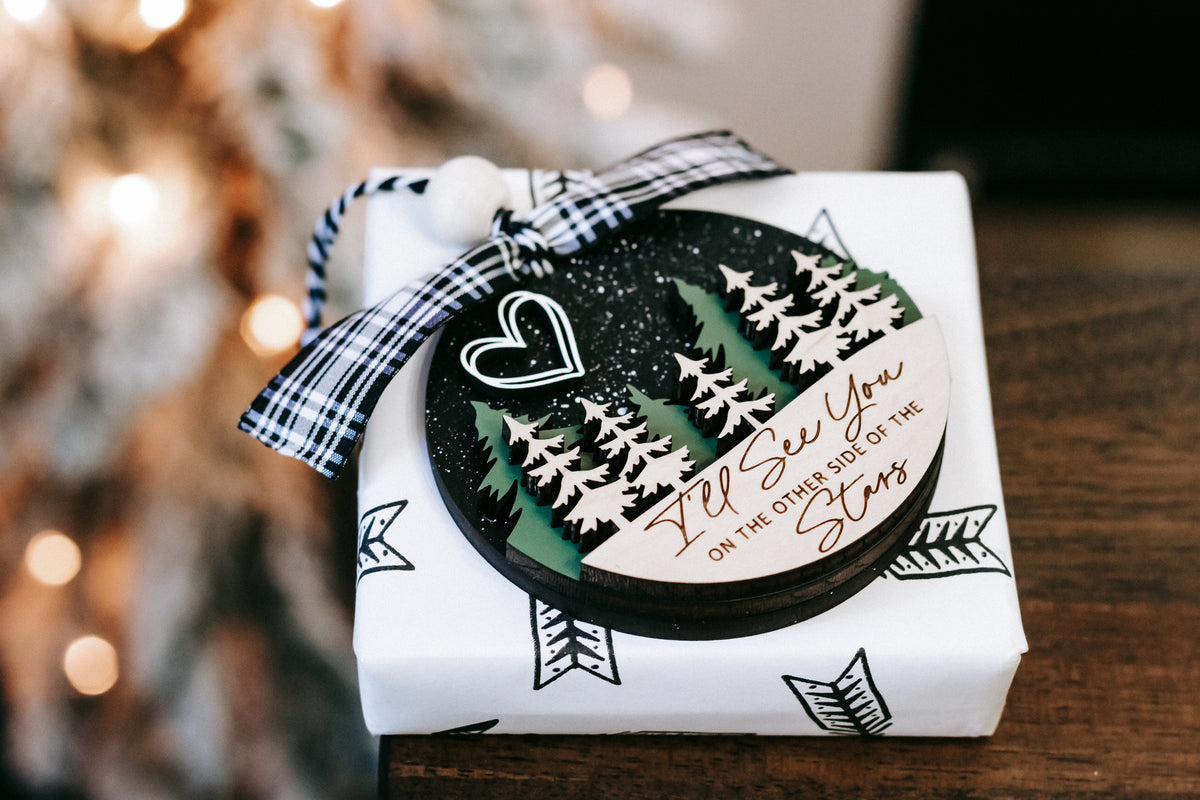 Wrapped memorial Christmas ornament with plaid ribbon bow and pine tree design on box.