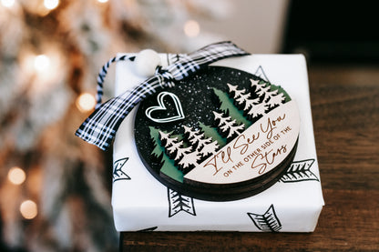 Wrapped memorial Christmas ornament with plaid ribbon bow and pine tree design on box.