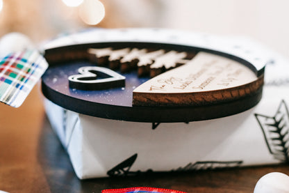 Gift-wrapped box with round memorial ornament disc, dark rim and printed tree design.